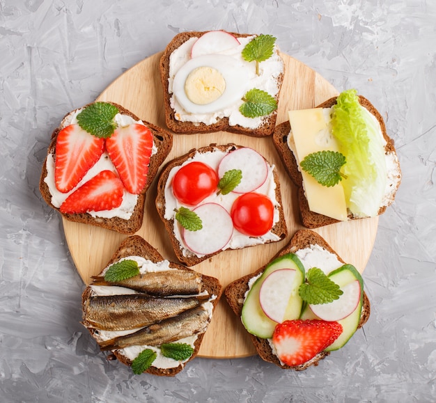 Set di diversi panini con formaggio, ravanello, lattuga, fragola, spratti, pomodori e cetrioli