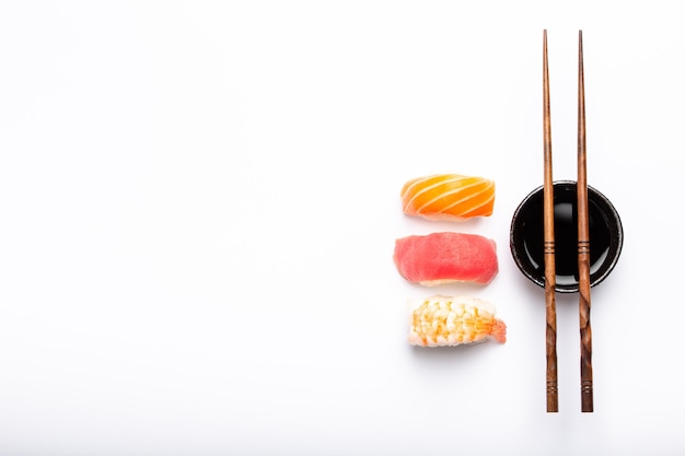 Set of different sushi nigiri, soy sauce and chopsticks over white background with copy space, top view. Traditional Japanese sushi concept, close-up