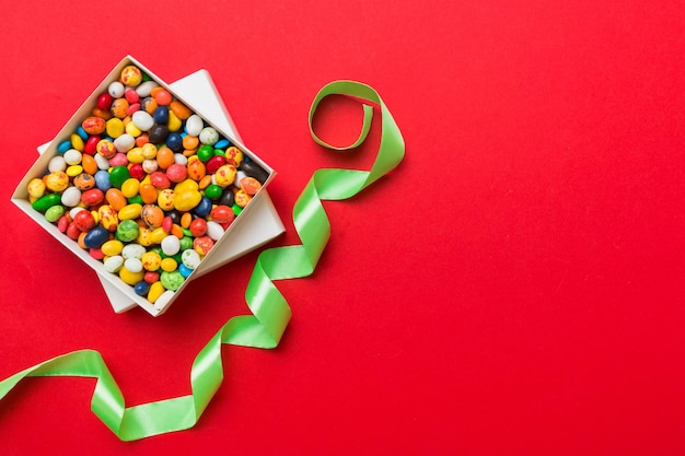 Set of different sweet candy in a paper box with a satin ribbon on a colored background Holiday concept