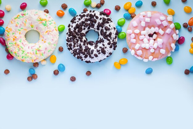 Set of different sweet glazed donuts with sprinkles and candy on blue background