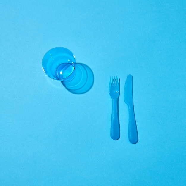 Set di utensili in plastica usa e getta e bicchiere vuoto con ombre su uno sfondo blu pastello, copia dello spazio. vista dall'alto