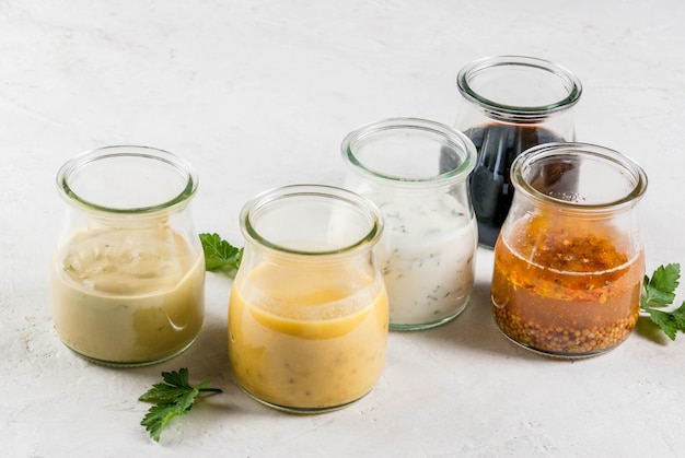 Set dressings voor salade: sausvinaigrette, mosterd, mayonaise of ranch, balsamico of soja, basilicum met yoghurt. donker witte betonnen tafel. kopieer ruimte bovenaanzicht