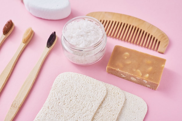 Set of eco friendly personal hygiene objects on a pink surface. Bamboo toothbrush, wooden comb, sponge, soap and sea salt, top view flat lay. Zero waste concept