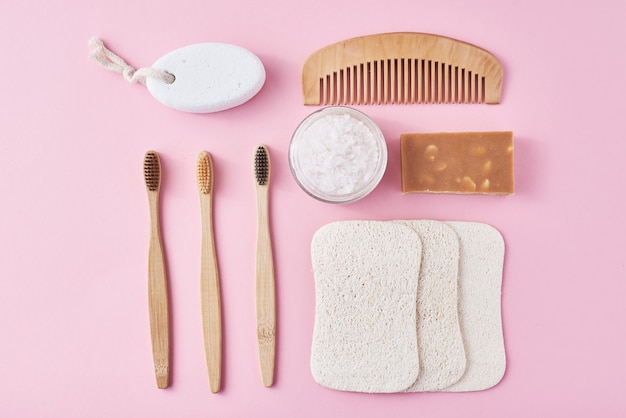 Set of eco friendly personal hygiene objects on a pink surface. Bamboo toothbrush, wooden comb, sponge, soap and sea salt, top view flat lay. Zero waste concept