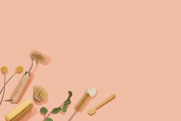 Set of eco friendly zero waste sustainable recyclable cleaning brushes and accessories with green eucalyptus and yellow flower ball on pink background. alternative household chores. natural living