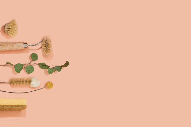 set of eco friendly zero waste sustainable recyclable cleaning brushes and accessories with green eucalyptus and yellow flower ball on pink background. alternative household chores. natural living.