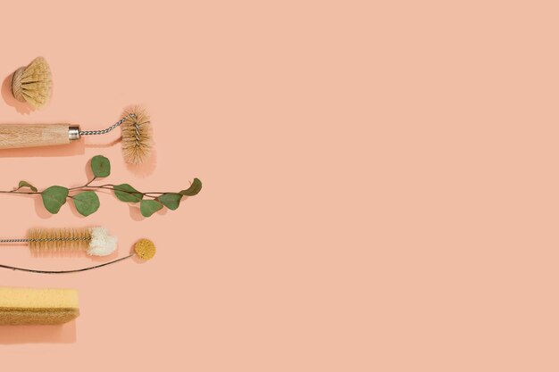 Set of eco friendly zero waste sustainable recyclable cleaning brushes and accessories with green eucalyptus and yellow flower ball on pink background. Alternative household chores. Natural living.