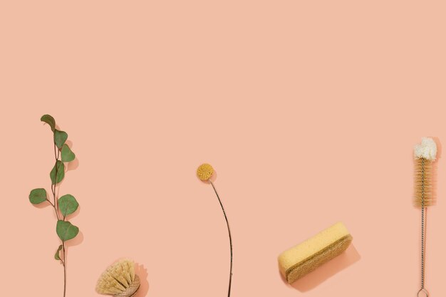 set of eco friendly zero waste sustainable recyclable cleaning brushes and accessories with green eucalyptus and yellow flower ball on pink background. alternative household chores. natural living.