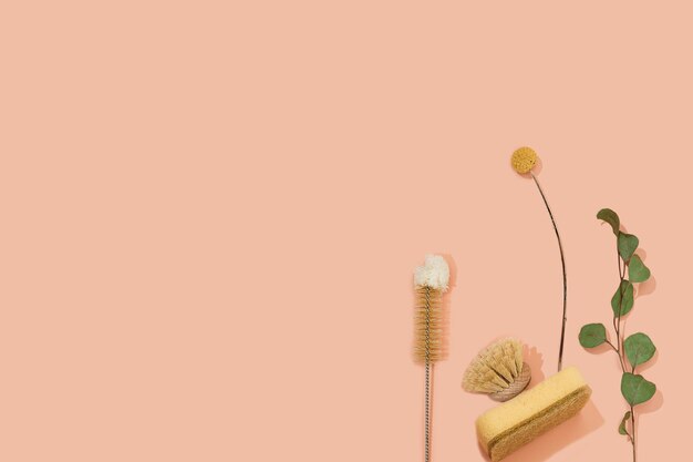 set of eco friendly zero waste sustainable recyclable cleaning brushes and accessories with green eucalyptus and yellow flower ball on pink background. alternative household chores. natural living.