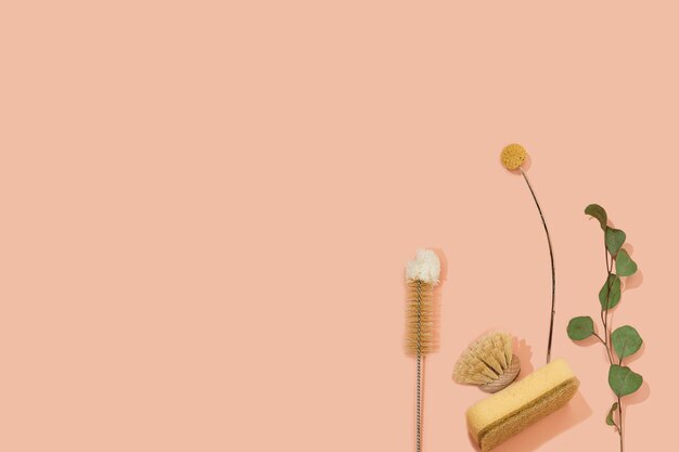 Set of eco friendly zero waste sustainable recyclable cleaning brushes and accessories with green eucalyptus and yellow flower ball on pink background. Alternative household chores. Natural living.