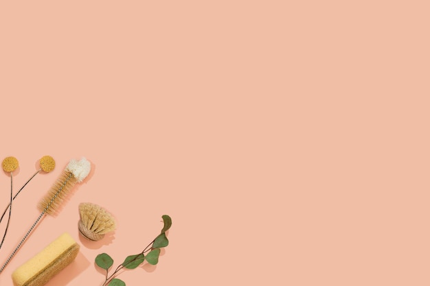 set of eco friendly zero waste sustainable recyclable cleaning brushes and accessories with green eucalyptus and yellow flower ball on pink background. alternative household chores. natural living.