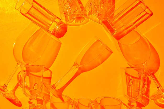 Set of empty drink glasses with shadows and sun highlights in the sunset light. Glassware arranged on an orange background with shadows. Top view