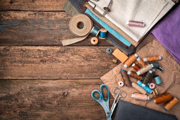 A set of fabrics, threads and other sewing accessories on a wooden background.