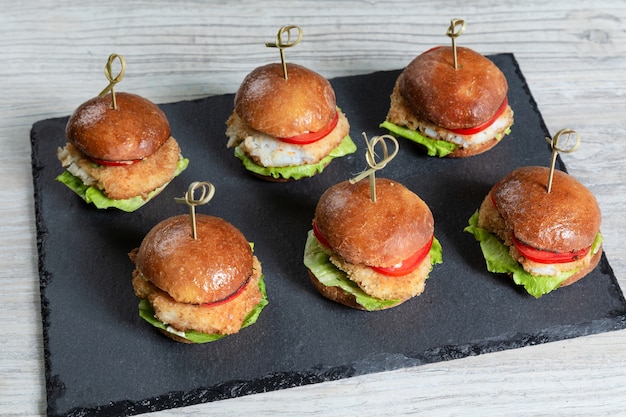 Set of fish burgers on black board on wooden table