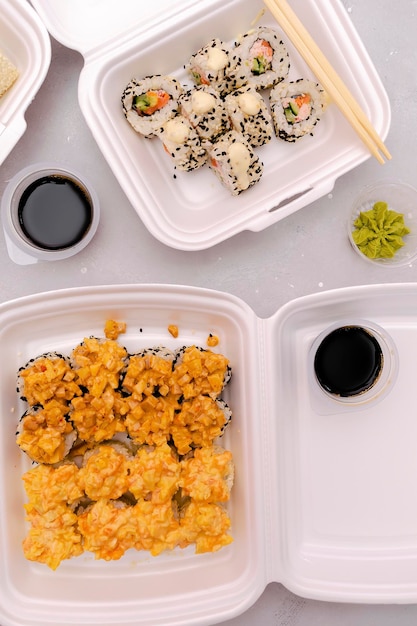 Set of fish sushi rolls with salmon and sesamegingerwasabisoy sauce packed in plastic disposable container box on gray backgroundSeafoodFood deliverytake out service from restaurant concept