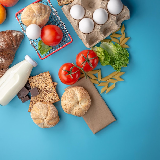 Set of fresh products and a miniature shopping basket on a blue background top view. Online shopping concept, food delivery.