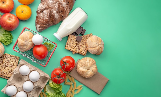 Set of fresh products and a miniature shopping basket on a green background top view. Online shopping concept, food delivery. Copy space.