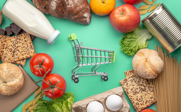 Set of fresh products and a miniature shopping cart on a green background top view. Online shopping concept, food delivery