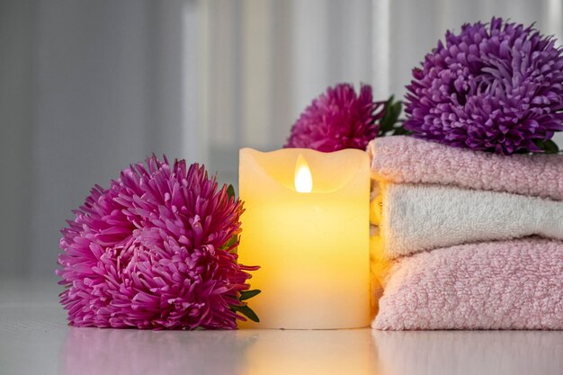 Набор свежих полотенец розового и белого цвета с фиолетовыми цветами астры и свечой на белом столе. Медитация и гармония, дзэн-подобная концепция.