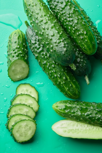 Set of fresh whole and sliced cucumbers on a green background with water drops. Garden cucumber wallpaper backdrop design