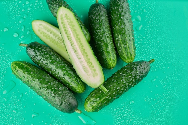 Set of fresh whole and sliced cucumbers on a green background with water drops. Garden cucumber wallpaper backdrop design