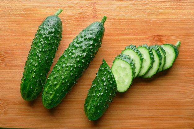 Set of fresh whole and sliced cucumbers on a wooden board.