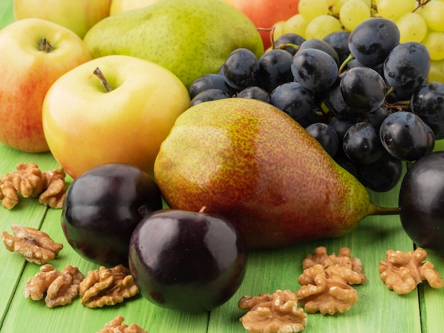 緑の木製のテーブル - リンゴ、ナシ、ブドウ、プラム、クルミの果物のセット