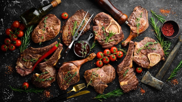 Set gegrilde steaks op een zwarte stenen tafel met specerijen en kruiden. Bovenaanzicht. Vrije ruimte voor uw tekst.