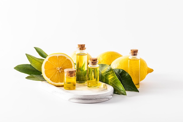 A set of glass bottles with a cork with a product based on lemon essential oil stand on a white plaster tray among lemons and leaves