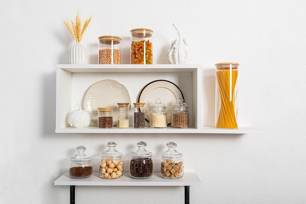 A set of glass and ceramic dishes glass filled jars with bulk products on white kitchen shelves on textured wall compact storage Stylish design