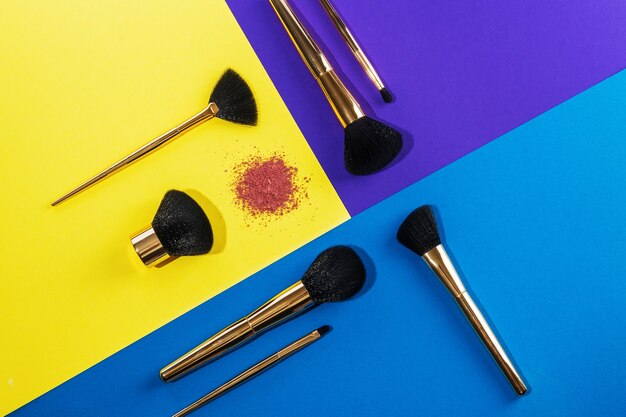 A set of gold brushes for applying makeup and eye shadow on the eyelid is on a color background, top view: design concept, make-up, beauty salon