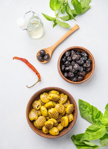 A set of green grill and black dried olives in wooden bowls on a light background with olive oil and basil The concept of vegetarian healthy snacks Top view and copy space