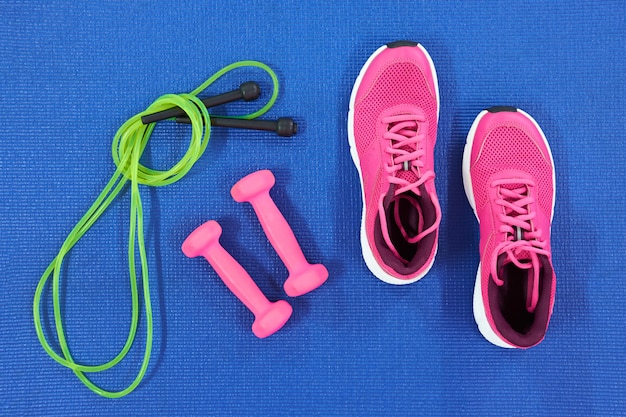 Set of green jump rope, sneakers and pink dumbeells, top view