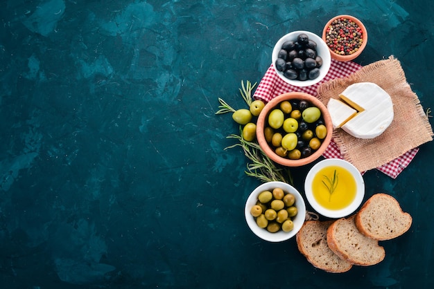 A set of green olives and black olives bread cheese and spices\
on a black stone table free space for text