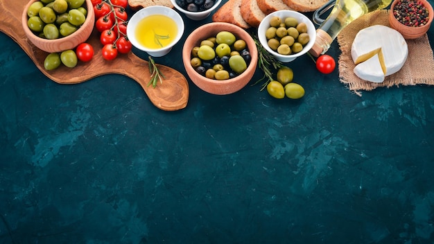 A set of green olives and black olives bread cheese and spices On a black stone table Free space for text