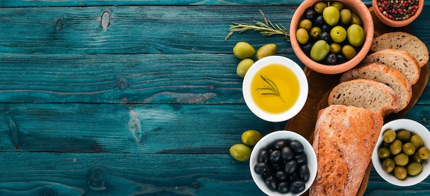 Набор зеленых оливок и черных оливок и закусок на синем деревянном столе Свободное место для текста