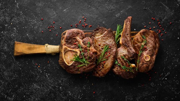 Set of grilled steaks on a black stone table with spices and herbs. Top view. Free space for your text.