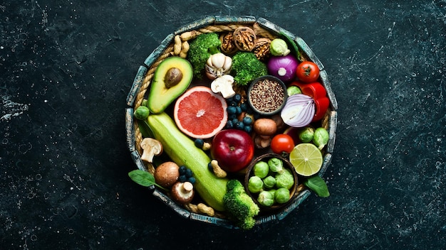 Set of healthy food in a wooden box Green vegetables avocado broccoli nuts mushrooms berries and spinach On a black stone background Top view Copy space