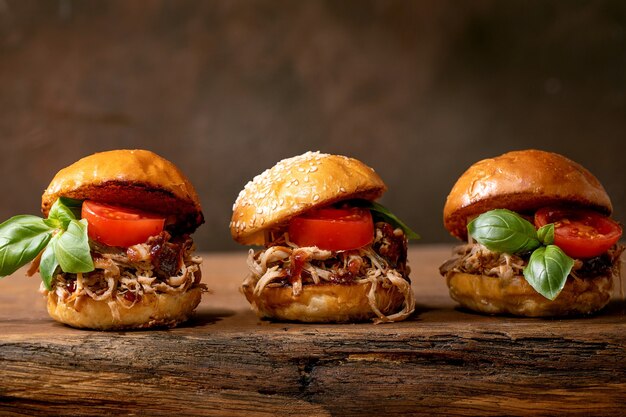 Set of homemade mini hamburgers in row with stew beef, tomatoes and basil on wooden background. Modern delicious fast food