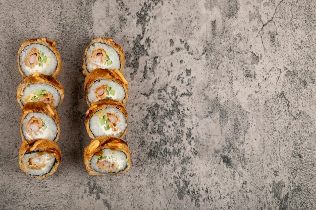 Set of hot fried sushi rolls with salmon on stone table. 