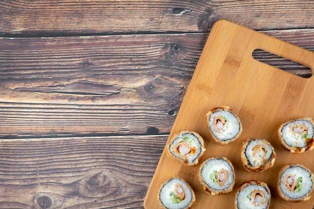 Set of hot fried sushi rolls with salmon on wooden board. 