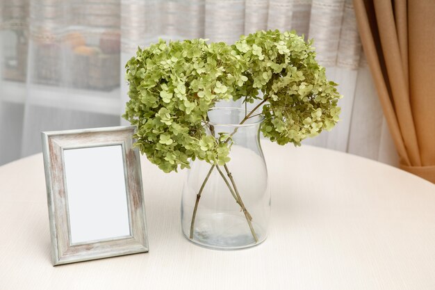 Set of hydrangea flowers and blank photo frames on white wooden table