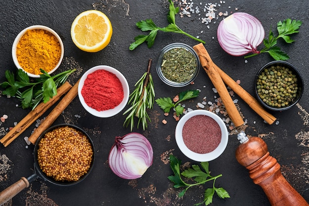 Set of Indian fragrant spices and herbs on a black stone background. Turmeric, dill, paprika, cinnamon, saffron, basil and rosemary in a spoon. Top view. Mock up.