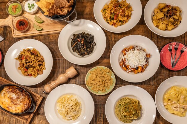 Foto set di piatti italiani con pasta alla parmigiana melanzane di tutti i tipi con pesto alla bolognese con salsa nera e frutti di mare su tavola di legno massello con pepiera e foglie di basilico