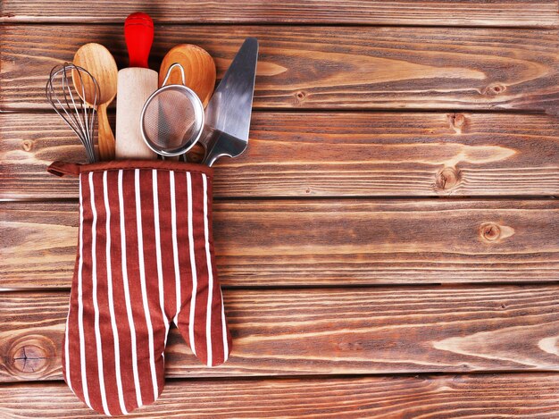 Set of kitchen utensils in mitten on wooden planks background