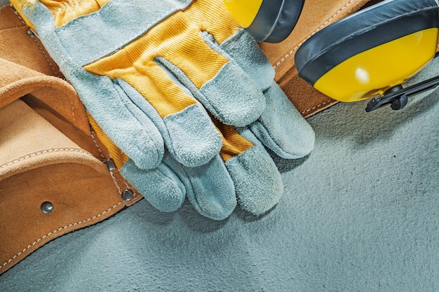 Set lederen gereedschapsgordel beschermende handschoenen oorbeschermers op betonnen ondergrond.