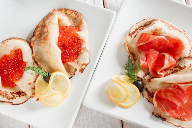 Set of luxury pancakes with seafood. Top view on white plates. Russian traditional salty crepes with seafood. 