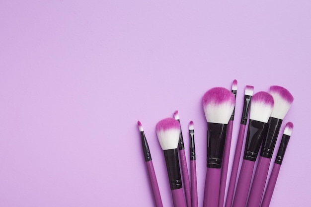 Set of makeup brushes on violet background flat lay