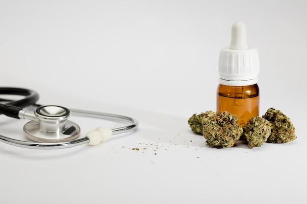 set of marijuana buds with dosing bottle stethoscope white background