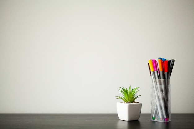 Set of markers in a plastic cup on wood table.